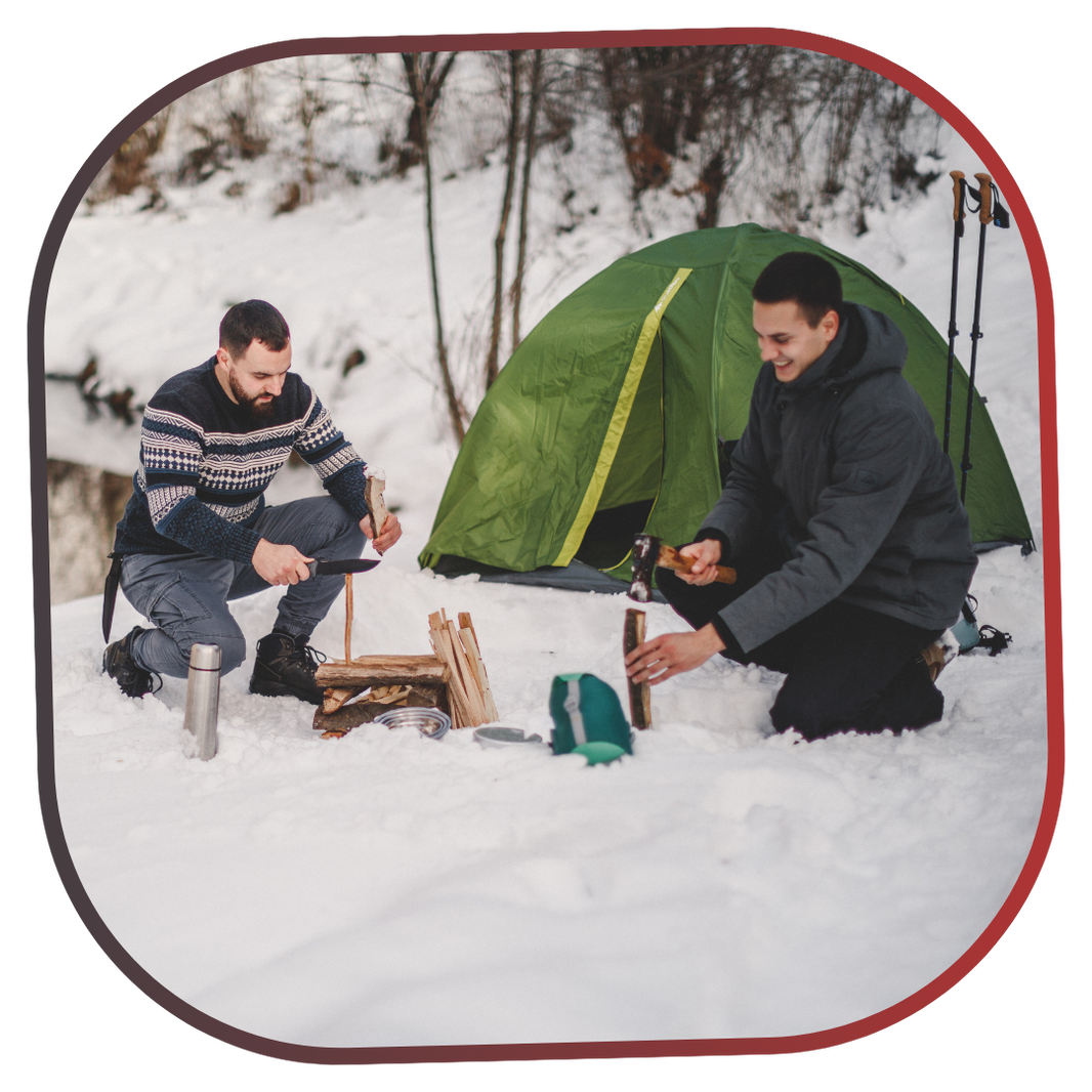 Two people camping in the snow with a green tent.